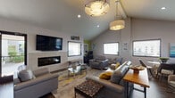 This thoughtfully designed single-floor space offers a versatile layout suited for both relaxation and productivity. The main lounge area is anchored by soaring vaulted ceilings and a linear tiled fireplace, with a wall-mounted flat-screen television above. Contemporary pendant lighting illuminates the room, which features dark hardwood flooring, a patterned area rug with yellow accents, and a mix of modern grey leather and upholstered seating. Multiple windows with blinds allow natural light to fill the space.

A dedicated workspace features a bold blue accent wall, a built-in desk with dual workstations, flanking open shelving, and comfortable lounge chairs—ideal for focused work or casual meetings. Vaulted ceilings continue here, reinforcing the open, airy character throughout.

The kitchenette is well-equipped with crisp white cabinetry, dramatic dark granite countertops, a mosaic tile backsplash, stainless steel sink, built-in microwave, and coffee station. Horizontal clerestory windows provide natural light while maintaining privacy. Together, these areas create a cohesive, modern environment designed for comfort and function.