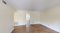 Located at 1655 Central Dr in Southern Pines, NC, this single-floor, 2-bedroom, 1-bathroom home offers a practical and comfortable layout. Wood-look flooring runs consistently throughout the entire space, giving each room a cohesive, clean appearance.

The living room is a welcoming entry point, characterized by a distinctive red front door and a window that lets in natural light, creating a bright and open feel. The space connects seamlessly to the rest of the home through a central hallway.

The kitchen features warm-toned oak cabinetry with ample upper and lower storage, light granite-style countertops, and white appliances including a refrigerator, electric range, and sink. A window above the range adds natural light to the workspace.

The primary bedroom is a generously sized room offering two closets — including a large bifold closet — a window with outdoor views, and textured ceilings. The second bedroom is comparably comfortable, with a window overlooking lush greenery and easy access to the hallway. A third room with built-in closet shelving provides additional flexible space.

The full bathroom includes a clean, white tub-shower combo with built-in shelving and chrome fixtures. Throughout the home, neutral cream-toned walls and textured ceilings provide a calm, understated backdrop suitable for a variety of interior styles.