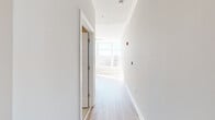 This thoughtfully designed single-floor unit offers a bright, contemporary living experience with clean lines, light hardwood flooring, and crisp white walls throughout. A welcoming hallway connects the spaces and houses a stacked in-unit washer and dryer for added convenience. Crown molding and recessed lighting lend an elevated feel to the interior.

The main living area is bathed in natural light from expansive floor-to-ceiling windows that frame sweeping urban skyline and hillside views, creating an open, airy atmosphere. A ceiling fan adds comfort to the sunlit space, which also features a built-in closet.

The kitchen is efficiently laid out and well-equipped, showcasing deep green shaker-style cabinetry, granite-look countertops with a tile backsplash, and a full suite of stainless steel appliances including a gas range, microwave, and refrigerator. Light hardwood flooring continues seamlessly from the main area into the kitchen.

The bathroom is a standout feature, finished with striking horizontal-striped tile work covering the walls, floor, and walk-in shower enclosure. A frameless glass shower door, a modern floating vanity, and a soaking tub complete the spa-inspired design, offering a refined and serene retreat within this compact yet functional space.