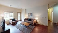 This single-story residence is thoughtfully laid out to maximize functionality and comfort across its various rooms. The living area serves as the heart of the space, featuring rich hardwood flooring, neutral walls, and natural light streaming through sliding windows and a glass-paneled door that provides outdoor views and easy access. The open layout accommodates a comfortable seating arrangement centered around an entertainment console, creating a relaxed yet organized atmosphere.

The kitchen is well-appointed with warm cherry wood cabinetry, granite countertops, and a full suite of stainless steel appliances, including a range, over-the-range microwave, and refrigerator with ice maker. A dedicated office or flex room offers plush carpeting, a large window with outdoor views, and ample space for a workstation. The bedroom connects to a walk-in closet with wire shelving for organized storage, while the bathroom features a granite-topped vanity with cherry wood cabinetry, a tub-shower combination, and tile flooring.

Completing the space is a spacious attached garage with a mounted automatic opener, concrete flooring, and high ceilings, offering generous vehicle and storage capacity.