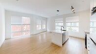 Located at 517 N Shipley St in Wilmington, Delaware, this single-floor residence offers a clean, modern aesthetic defined by crisp white walls, light wood-tone flooring, and thoughtfully selected finishes. The open-concept living and kitchen area serves as the heart of the space, flooded with natural light through multiple large windows fitted with blinds. The kitchen is outfitted with sleek, handle-free white cabinetry, a white quartz island with an integrated sink and dishwasher, stainless steel appliances including a range, microwave, and refrigerator, and track lighting overhead. The seamless flow into the living area creates a bright, airy atmosphere well-suited for both everyday living and entertaining. Bedrooms feature the same warm wood-tone flooring and large windows that invite natural light and neighborhood views. The primary bathroom is a standout, offering a double-sink vanity with white cabinetry and quartz countertops, a walk-in glass-door shower with large-format tile, matte black fixtures, and recessed lighting. A secondary full bathroom includes a soaking tub and shower combination with coordinating tile and matte black hardware. A clean hallway connects the living spaces, finished with recessed lighting and white interior doors, reinforcing the cohesive, minimalist design language found throughout the unit.