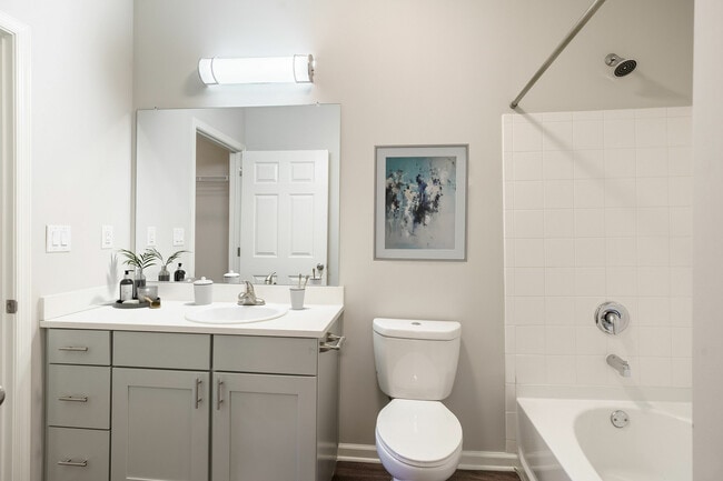 Modern bathroom with sleek white cabinetry, elegant wall art, and a bathtub for relaxation. - Apartments at Glenmoore