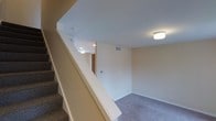 This three-floor property offers a practical and well-organized layout designed to maximize usable living space across each level. The interior is finished with neutral, warm-toned walls that create a clean and inviting atmosphere throughout. Carpeted flooring adds comfort underfoot in the lower-level areas, while flush-mount and recessed ceiling fixtures provide consistent, even illumination across the space. The staircase, finished with matching carpet and a clean white railing, serves as the central connecting element between floors, offering easy access to each level. HVAC venting is integrated into the walls and ceilings, reflecting a thoughtfully planned infrastructure. The lower level presents an open area with ample room for flexible use, whether as a recreation room, additional living space, or storage. Doorways lead to additional rooms, hinting at a well-compartmentalized floor plan. The overall design is straightforward and move-in ready, with a neutral palette that accommodates a wide range of interior styles. The consistent finishes across the space give it a cohesive, well-maintained appearance suitable for everyday living.