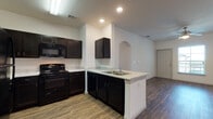 Located at 5215 S Raul Longoria Rd in Edinburg, Texas, this single-floor unit offers a thoughtfully designed open-concept layout that seamlessly connects the kitchen and living areas. The kitchen is a standout feature, equipped with dark espresso cabinetry, light stone-look countertops, a peninsula with a double-basin sink, and black appliances including a gas range, built-in microwave, dishwasher, and refrigerator. A distinctive arched doorway adds architectural charm, framing the transition between the kitchen and the spacious living area. Wood-look plank flooring runs throughout the main living spaces, lending a warm and cohesive feel, while ceiling fans provide both comfort and style. The bedrooms are generously sized, with one featuring plush carpeting and a window that brings in natural light, and another with wood-look flooring and a ceiling fan. The bathrooms are clean and functional, featuring dark vanity cabinetry, white countertops, large mirrors, and wood-look flooring. The full bathroom includes a tub-shower combination. Additional storage is available via closets conveniently positioned near the living and bedroom areas. The overall design is modern and neutral, creating a bright and welcoming living environment.