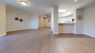 This single-floor residence offers a thoughtfully designed layout that balances open communal spaces with comfortable private retreats. The expansive living area is a standout feature, showcasing light wood-look flooring, crown molding, and a decorative column that elegantly separates the space. A large sliding door allows natural light to pour in, creating a bright and airy ambiance throughout. The open-concept kitchen connects seamlessly to the living area via a breakfast bar counter. It is outfitted with crisp white cabinetry, ample counter space, and a full suite of white appliances, including a refrigerator and electric range. The bedrooms feature warm, neutral-toned carpeting and windows fitted with blinds that allow for controlled natural light, offering a calm and restful environment. The space includes two full bathrooms — one featuring a soaking tub with a shower curtain enclosure, a white vanity, and wood-look flooring, and a second more compact bathroom with a single vanity and mirror. A dedicated laundry area houses a full-sized side-by-side washer and dryer, adding everyday convenience. Throughout, the neutral color palette, clean white trim, and consistent finishes contribute to a cohesive and welcoming atmosphere.