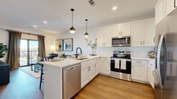 Located at 8707 Shawnee Mission Pkwy in Merriam, Kansas, this thoughtfully designed one-bedroom, one-bathroom residence offers a modern, cohesive aesthetic throughout its efficiently utilized single-floor layout. Warm hardwood-style flooring flows continuously through each room, lending a sense of unity and warmth to the space.

The kitchen serves as a centerpiece, featuring crisp white shaker cabinetry, white quartz countertops, and a full suite of stainless steel appliances including a refrigerator, electric range, microwave, and dishwasher. A peninsula island with seating for multiple guests provides both additional prep space and a casual dining area, illuminated by stylish pendant lighting overhead.

The living room is bright and inviting, benefiting from large sliding glass doors that open to a private balcony with exterior views, allowing generous natural light to fill the space. The bedroom offers a comfortable and serene retreat, with a well-sized window framing outdoor views and a ceiling fan overhead.

The bathroom is finished in a clean, modern style with a white vanity, undermount sink, matte black fixtures, and an LED-lit mirror. A dedicated laundry room houses a full-size washer and dryer alongside a water heater and HVAC unit, adding practical convenience. A separate closet rounds out the home's functional layout.