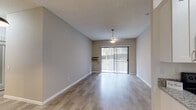 Located at 5155 Luigi Terrace in San Diego, Unit #40 is a single-floor residence designed with a clean, modern aesthetic and a functional layout. The open living area is a highlight of the unit, featuring light wood-style flooring, neutral gray walls, a textured ceiling, and a ceiling fan. A full-width sliding glass door with vertical blinds floods the space with natural light and provides access to an outdoor area with greenery views. The kitchen is laid out in a galley style, outfitted with white shaker cabinets, granite countertops, a stainless undermount sink, and black appliances including a refrigerator, range, and microwave. A pendant light fixture adds a finishing touch to the dining area just outside the kitchen. The bedrooms feature plush carpeting, ceiling fans or pendant lighting, and windows that bring in natural light with views of surrounding foliage. The bathroom includes a white vanity with granite countertops, dual mirrors, and a tub-shower combination. A separate water closet with wood-style tile flooring adds an additional layer of privacy and convenience. Throughout the unit, clean white baseboards and neutral tones create a cohesive, well-maintained living environment.