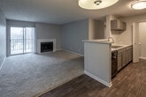 This single-floor residence offers a thoughtfully designed layout with a variety of functional living spaces. The living room serves as the heart of the home, featuring soft wall-to-wall carpeting, a classic wood-burning fireplace with a clean white surround, and a sliding glass door that opens to a private balcony, allowing natural light to fill the space. A textured ceiling runs throughout the unit, adding a consistent design element across rooms.

The kitchen is open and efficiently arranged, featuring dark cabinetry with ample storage, black appliances including a refrigerator and gas range, a dishwasher, and a peninsula with a countertop sink that separates the kitchen from the dining area. Wood-look flooring anchors the kitchen and dining spaces, providing a practical and attractive contrast to the carpeted living areas.

The bedrooms are generously sized and carpeted, each equipped with ceiling fans with integrated lighting. One bedroom includes access to a walk-in closet, offering additional storage. The bathroom is well-appointed with a large vanity featuring a quartz-style countertop, a single basin sink with brushed nickel fixtures, a tub-shower combination with tile surround, and wood-look flooring. The overall color palette of neutral grays and whites creates a clean, modern atmosphere throughout.