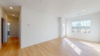 This single-floor unit offers a clean, modern aesthetic defined by crisp white walls, light-toned hardwood flooring, and an abundance of natural light throughout the main living areas. The open-concept living space is generously proportioned, featuring large windows and a glass-paneled entry door that invite sunlight deep into the interior, creating a warm and airy atmosphere.

The kitchen is thoughtfully designed with taupe shaker-style cabinetry, light quartz countertops, a subway tile backsplash, and a full suite of stainless steel appliances including a gas range, microwave, and refrigerator. A peninsula with a breakfast bar provides additional prep space and a natural transition into the living area.

The bedrooms offer comfortable dimensions, with one room featuring soft wall-to-wall carpeting and recessed lighting. Two full bathrooms serve the unit: one includes a sliding glass-enclosed shower stall with marble-style tile flooring and a vanity with warm wood cabinetry, while the second features a combined tub and shower, a matching vanity, and the same elegant tile flooring. Throughout, the unit maintains a cohesive, contemporary palette that is both functional and visually appealing.