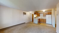 Located at 2389 South Southeast Boulevard in Spokane, WA, this single-floor unit offers a practical and functional layout spread across several well-defined living areas. The spacious living room is finished with wall-to-wall carpeting and features a textured ceiling, baseboard heating, and a wall-mounted air conditioning unit for year-round comfort. Natural light filters in through a sliding glass door and a separate French-style door, both providing access to an outdoor patio area with views of surrounding trees and neighboring structures. The kitchen is efficiently designed in an L-shaped configuration, outfitted with warm wood cabinetry, a white electric range, a double-basin sink, and a full-size refrigerator. Tile flooring in the kitchen provides a clean contrast to the carpeted living spaces. An additional carpeted room, accessible from the main living area, offers flexible use as a bedroom or den and includes a utility closet housing the water heater. The bathroom features a wood-cabinet vanity with ample counter space, a mirrored medicine cabinet, and a tiled tub-shower combination. Throughout the unit, neutral wall tones and consistent finishes create a cohesive, understated aesthetic suited for comfortable everyday living.