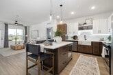 This thoughtfully designed 2-bedroom, 2-bathroom residence offers a seamless open-concept layout that connects the kitchen, dining area, and living room into one cohesive, light-filled space. Light hardwood flooring flows throughout the main areas, complementing a clean, contemporary aesthetic.

The kitchen is a standout feature, showcasing a two-tone cabinetry design with warm wood lower cabinets and crisp white upper cabinets, illuminated by under-cabinet LED lighting. A farmhouse-style sink, white quartz countertops, stainless steel appliances, and a central island with seating for multiple guests make this kitchen as functional as it is visually striking. Pendant lighting above the island adds an elegant finishing touch.

The living room is bright and welcoming, featuring a ceiling fan, large windows with outdoor views, and a sliding barn door that adds a modern architectural detail. A private outdoor access door extends the living space further.

The primary bedroom offers a comfortable retreat with plush carpet, a large window with natural light, and access to a well-organized walk-in closet complete with built-in shelving and hanging storage. The primary bathroom features dual vessel sinks, a long wood-toned vanity, illuminated mirrors, and a glass-enclosed shower.

Two dedicated closets and a hallway round out this efficiently planned and stylishly finished home.