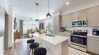 This thoughtfully designed single-floor residence showcases a seamless open-concept layout that connects the kitchen and living areas into one cohesive, light-filled space. The kitchen is a standout feature, outfitted with flat-front taupe cabinetry extending to the ceiling, a crisp white quartz countertop island with an undermount sink, stainless steel appliances including a French door refrigerator, range, microwave, and dishwasher, complemented by a tile backsplash. Stylish globe pendant lights hang above the island, adding a warm, modern touch. Wood-style flooring flows throughout the main living areas, anchoring the space with warmth and cohesion. The living room is bright and welcoming, with multiple windows that invite natural light and offer outdoor views, enhanced by a ceiling fan overhead. The bedrooms are carpeted for comfort, each featuring a ceiling fan, generous windows with horizontal blinds, and tray ceiling detailing that adds architectural interest. The bathroom is well-proportioned, featuring a wide vanity with ample storage, a backlit mirror, a soaking tub with shower combination, and rich wood-tone flooring that ties the design together. Throughout the space, clean lines and a neutral palette create a modern yet inviting ambiance.