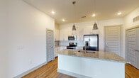 This single-story residence is designed with a clean, contemporary aesthetic throughout. The open-concept kitchen serves as a central highlight, showcasing a large island with granite countertops, an undermount sink, and stylish pendant lighting overhead. White cabinetry lines the walls alongside a mosaic tile backsplash, while stainless steel appliances — including a French door refrigerator, range, and built-in microwave — provide a polished, functional finish. Warm hardwood-style flooring flows through the kitchen and main living areas, where a ceiling fan, recessed lighting, and French doors invite natural light and outdoor access.

The bedrooms offer plush neutral carpeting, ceiling fans, and windows with blinds that allow for ample natural light. The primary bedroom connects directly to an en-suite bathroom featuring granite countertops, white cabinetry, a large framed mirror, a tiled walk-in shower, and access to a spacious walk-in closet. An additional bathroom echoes this refined design with matching granite surfaces, white vanity cabinetry, marble-style tile, and hardwood-style flooring. Throughout the unit, neutral tones and consistent finishes create a cohesive, modern atmosphere.