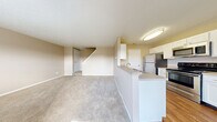 This two-bedroom, one-bathroom townhouse in Columbus, Ohio offers a practical and comfortable layout spread across two floors. The main level features an open-concept living, dining, and kitchen area, where wood-look flooring runs through the kitchen and transitions to plush carpet in the living and dining spaces. The kitchen is well-equipped with stainless steel appliances — including a refrigerator, electric range, microwave, and dishwasher — complemented by white cabinetry, light countertops, and a peninsula with a sink that overlooks the living area. A staircase leads from the main floor to the upper level. Natural light filters in through windows fitted with blinds, lending warmth to the neutral beige walls throughout. Upstairs, two carpeted bedrooms provide restful retreats, with the primary bedroom offering a generous footprint and a sliding double-door closet. The second bedroom includes a window with outdoor views. The full bathroom features a single-sink vanity with white cabinetry, a large mirror, and a tub-shower combo. Additional spaces include multiple closets, a laundry area, a utility room, and a hallway, ensuring ample storage and everyday functionality throughout the home.