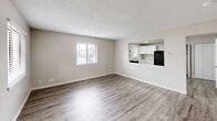 This two-story unit at 2635 S Topeka St in Wichita, Kansas offers 3 bedrooms and 2 bathrooms spread evenly across two floors. The main level features an open-concept living and kitchen area connected by a pass-through window, creating a bright and connected feel. The living room is finished with durable wood-look vinyl plank flooring, neutral warm-gray walls, and a textured ceiling, with a window dressed in horizontal blinds allowing in natural light. The kitchen is well-appointed with crisp white cabinetry, granite-patterned countertops, a stainless steel sink, and black appliances including a range and refrigerator. A staircase leads to the upper level, where all three bedrooms are located. Each bedroom features plush carpeted flooring, ceiling fans with light fixtures, and windows with blinds providing natural light and outdoor views. The spacious primary bedroom includes two closets for ample storage. The bathrooms echo the kitchen's aesthetic with white cabinetry, granite-patterned countertops, and framed mirrors. A dedicated closet and hallway round out the upper floor's practical layout. Throughout the unit, consistent neutral tones and clean finishes create a cohesive, move-in-ready atmosphere.