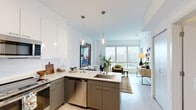 Located at 909 E Michigan St in Milwaukee, WI, this one-bedroom, one-bathroom unit offers a smartly designed open-concept layout that maximizes every square foot. Light hardwood flooring runs throughout, tying together a bright, cohesive interior illuminated by abundant natural light.

The kitchen is a functional centerpiece, featuring two-tone cabinetry—white uppers and gray lowers—paired with white quartz countertops, stainless steel appliances including a refrigerator, range, microwave, and dishwasher, and stylish pendant lighting overhead. It opens seamlessly into the living room, which is anchored by floor-to-ceiling windows offering sweeping views of the Milwaukee cityscape.

The bedroom is a calm, neutral retreat with clean white walls, a wall-mounted sconce, and a dedicated closet for storage. The full bathroom is finished with white subway tile in the walk-in shower, a gray vanity, and light flooring that maintains the unit's consistent modern aesthetic.

A keypad-secured entry door opens to a tidy foyer with in-unit stacked laundry nearby. Throughout, the design balances contemporary finishes with a warm, livable feel—making this a well-appointed urban residence in the heart of Milwaukee.