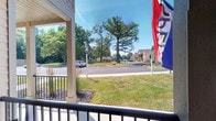 Located at 1655 Gilmore Park Ave in Columbus, Ohio, this single-story property sits within a well-kept residential community on the west side of the city. The exterior presents a clean, inviting aesthetic with a covered front porch area framed by dark railings, offering a comfortable vantage point overlooking the surrounding grounds. From this vantage point, residents and visitors can take in expansive views of neatly manicured lawns, mature trees, and a spacious parking area that serves the community. The landscaping reflects deliberate care, with ornamental grasses and fresh mulched beds adding texture and visual interest to the entryway. The broader community setting features neighboring multi-story buildings visible in the background, suggesting a mixed residential development with a cohesive architectural style characterized by neutral tones and traditional detailing. The open sky and abundant tree canopy contribute to an airy, pleasant atmosphere throughout the grounds. The single-floor layout of this particular property offers ease of accessibility, making it a practical and comfortable option within this established Columbus neighborhood community.