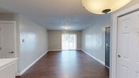 Located at 4935 Brock St in Indianapolis, Indiana, this single-floor residence offers a well-organized and functional layout with a consistent, neutral design palette throughout. The open living area is characterized by rich, dark hardwood-style flooring that extends throughout the main living spaces, complemented by soft gray walls and clean white baseboards. A sliding glass door floods the living area with natural light and provides direct views of the surrounding outdoor greenery, creating a bright and inviting atmosphere.

The kitchen is a practical and well-appointed space, featuring warm medium-toned wood cabinetry with ample upper and lower storage, white countertops, and black appliances including a gas range, over-the-range microwave, and dishwasher. A peninsula counter adds additional workspace and serves as a natural divider between the kitchen and living areas.

The bedrooms offer plush carpeted flooring for added comfort. One bedroom includes a ceiling fan, a window for natural light, and a walk-in closet with wire shelving for organized storage. The full bathroom is neatly finished with a wood-toned vanity, a large mirror with overhead lighting, and a tub-shower combination with clean white surrounds and hardwood-style flooring. The overall ambiance of this residence is clean, practical, and move-in ready.