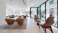 Located at 222 M St SW in Washington, DC, this single-floor amenity space presents a refined, contemporary interior defined by clean lines, warm material palettes, and thoughtfully arranged functional zones. Light-toned large-format tile and wood flooring flow throughout, unifying the open layout and enhancing the sense of spaciousness.

The main lounge area is anchored by floor-to-ceiling glass walls that flood the space with natural light and provide open views to the exterior. Curved caramel leather lounge chairs and modular seating arrangements create an inviting, social atmosphere suited for both casual gatherings and quiet relaxation.

A well-appointed wet bar and kitchenette area features warm walnut cabinetry, a dark backsplash, under-counter appliances, and dual mounted screens—ideal for entertaining. Adjacent to this, a dramatic bar-height table with glass top and mesh counter stools sits beneath a row of modern cylindrical pendant lights, reinforcing the space's upscale character.

A cozy built-in banquette nook offers an intimate dining setting, complete with upholstered bench seating, accent pillows, a round glass-top table, and a geometric overhead light fixture. A dedicated game area with a shuffleboard table and illuminated wall-mounted shelving rounds out the amenities, adding a recreational dimension to this polished communal environment.