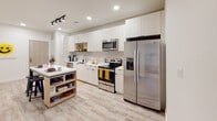 Located at 1201 Snyder Lane in Blacksburg, Virginia, this contemporary single-floor unit offers a thoughtfully designed layout suited for shared living. The kitchen stands out with its floor-to-ceiling light wood cabinetry, white quartz countertops, stainless steel appliances including a refrigerator, range, microwave, and dishwasher, plus recessed and track lighting overhead. Light wood-style flooring flows throughout, lending a cohesive and modern aesthetic to the entire space.

The living area is bright and open, featuring a large window with roller shades that allows natural light to fill the room. A sectional sofa, media console, and colorful wall art create a welcoming, functional gathering space.

Multiple bedrooms offer individual retreats, each with neutral-toned accent walls, wood-framed beds, dedicated desk and workspace areas, and windows with roller shades providing privacy and light control. The bathrooms are clean and modern, with white undermount sinks, large mirrors, and walk-in closet access directly from the bathroom corridor — a practical feature for each resident. The overall ambiance is fresh, bright, and well-organized, making this an ideal living environment near Virginia Tech.