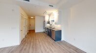 Located in the vibrant Capitol Riverfront neighborhood of Washington, DC, this single-floor residence at 1250 Half St SE offers a thoughtfully designed, modern living environment. The open-concept layout connects the kitchen and living area seamlessly, with light wood-tone flooring flowing throughout and crisp white walls that contribute to a bright, airy atmosphere.

The kitchen is a standout feature, equipped with a full suite of stainless steel GE appliances — including a French door refrigerator with ice and water dispenser, an electric range, built-in microwave, and dishwasher. Two-tone cabinetry pairs deep navy-blue lower cabinets with white upper cabinets, complemented by a stone-look countertop and a subtle tile backsplash, creating a polished, contemporary aesthetic.

The living area is bathed in natural light through floor-to-ceiling black-framed windows and a glass exterior door, offering views of the surrounding urban landscape. The space provides a clean, open canvas ideal for a variety of furniture arrangements.

The full bathroom is finished with large-format light tile flooring, a dark-cabinetry vanity topped with a vessel sink and stone countertop, a wide mirror with overhead lighting, and a full soaking tub and shower combination with clean white tile surround. The overall design throughout prioritizes modern finishes, functionality, and a neutral palette.