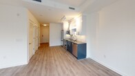 Located in the vibrant Capitol Riverfront neighborhood of Washington, DC, this single-floor residence at 1250 Half St SE offers a thoughtfully designed, modern living environment. The open-concept layout connects the kitchen and living area seamlessly, with light wood-tone flooring flowing throughout and crisp white walls that contribute to a bright, airy atmosphere.

The kitchen is a standout feature, equipped with a full suite of stainless steel GE appliances — including a French door refrigerator with ice and water dispenser, an electric range, built-in microwave, and dishwasher. Two-tone cabinetry pairs deep navy-blue lower cabinets with white upper cabinets, complemented by a stone-look countertop and a subtle tile backsplash, creating a polished, contemporary aesthetic.

The living area is bathed in natural light through floor-to-ceiling black-framed windows and a glass exterior door, offering views of the surrounding urban landscape. The space provides a clean, open canvas ideal for a variety of furniture arrangements.

The full bathroom is finished with large-format light tile flooring, a dark-cabinetry vanity topped with a vessel sink and stone countertop, a wide mirror with overhead lighting, and a full soaking tub and shower combination with clean white tile surround. The overall design throughout prioritizes modern finishes, functionality, and a neutral palette.