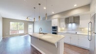 Located at 2420 Cardinal Drive in San Diego, CA, this thoughtfully designed two-bedroom, one-bathroom residence offers a clean, modern aesthetic across a single floor. The open-concept kitchen and living area serves as the heart of the home, anchored by a large center island with a quartz countertop, double undermount sink, and seating overhang. Elegant pendant lighting hangs above the island, complementing recessed ceiling lights throughout. The kitchen features crisp white shaker cabinetry, a sleek stainless steel wall-mounted range hood, subway tile backsplash, and stainless steel appliances including a built-in microwave, double wall oven, and full-size refrigerator. Rich hardwood-style flooring flows seamlessly through the living areas and bedrooms, adding warmth to the neutral gray-toned walls. The living room benefits from abundant natural light via large windows and a sliding glass door, and is equipped with a ceiling fan. Both bedrooms are well-proportioned, bright, and include ceiling fans, with the primary bedroom offering a dedicated closet. A hallway connects the private areas of the home. The bathroom features a quartz-topped vanity, a framed mirror, and tile flooring. Clean white trim and a consistent modern palette unify the entire space.