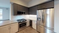 Located on West Pico Boulevard in Los Angeles, this modern single-floor unit showcases a clean, contemporary design with light wood-style flooring and a neutral color palette throughout. The open-concept kitchen is a standout feature, equipped with stainless steel appliances including a gas range, over-the-range microwave, and a French door refrigerator with water dispenser. Two-tone cabinetry — dark upper and light lower — pairs with a striking chevron-patterned tile backsplash and a built-in wine cooler. A peninsula with a light quartz countertop and an integrated sink connects the kitchen to the main living area. The spacious living area benefits from recessed lighting and dual windows that invite natural light and offer city views. Bedrooms feature large windows with views of the surrounding neighborhood and sliding-door closets with built-in hanging storage. Two full bathrooms are finished with wood-look flooring, tub-shower combos with white subway tile surrounds, and accessible grab bars for added convenience. Recessed lighting and clean wall finishes carry throughout, giving the entire space a bright, well-maintained, move-in-ready feel.