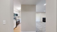 This single-floor, 2-bedroom, 2-bathroom residence offers a practical and comfortable layout across a well-utilized footprint. The open-concept kitchen and living area serves as the heart of the home, where a sleek kitchen features white shaker cabinetry with gold hardware, stainless steel appliances including a refrigerator, range, and over-the-range microwave, and a peninsula with a striking marble-style quartz countertop and an undermount sink — ideal for casual dining or entertaining. Light wood-style flooring runs through the kitchen, transitioning into plush carpeting in the living room, which is anchored by a classic black-surround fireplace and a ceiling fan, creating a cozy and inviting atmosphere. Natural light filters through vertical blinds and windows throughout the space. The primary bedroom is a comfortable retreat with soft carpeting, recessed lighting, and a window with a view of surrounding greenery. The bathrooms are finished with marble-style quartz countertops, white cabinetry with gold hardware, and wood-style flooring. A dedicated laundry area accommodates a full-size side-by-side washer and dryer with overhead shelving for added storage. Two closets and two hallways complete the functional layout of this well-designed residence.