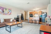 Located at 234 N Prince St in Whitewater, Wisconsin, this single-floor, one-bedroom, two-bathroom unit offers a practical and well-organized layout. The open-concept living and kitchen area forms the heart of the space, where warm wood-tone cabinetry, light countertops, and black appliances — including a range, built-in microwave, dishwasher, and refrigerator — are complemented by a peninsula with bar-stool seating, ideal for casual dining. Light wood-look flooring anchors the kitchen zone, which transitions seamlessly into the carpeted living area. The living room is generously proportioned, featuring large windows that draw in natural light and provide views of the surrounding neighborhood. The private bedroom offers a cozy, carpeted retreat with a window fitted with blinds, an open wardrobe closet, and space for a desk. Two bathrooms serve the unit; one is notably spacious, featuring a wide dual-sink vanity with rich wood cabinetry, a large mirror, and tile flooring. The second bathroom includes a shower/tub combination. Neutral wall tones throughout provide a clean, versatile backdrop, while the overall layout maximizes functionality within a compact and efficient footprint.