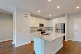 Located at 7105 Hall Rd in Union City, GA, this well-appointed 2-bedroom, 2-bathroom single-floor residence offers a clean, contemporary design with thoughtful finishes throughout. The heart of the home is an open-concept living, dining, and kitchen area bathed in natural light, anchored by a central kitchen island with a granite countertop and undermount sink. The kitchen is equipped with stainless steel appliances — including a range, microwave, and refrigerator — complemented by crisp white shaker cabinetry and matching granite countertops along the perimeter. Rich hardwood-style flooring runs throughout the entire residence, adding warmth and continuity. The living area opens to the outdoors through elegant French doors, allowing abundant natural light and outdoor views. Both bedrooms are generously sized, each featuring large windows with outdoor views and ceiling fans for comfort. The primary bedroom connects to a well-designed en-suite bathroom with a granite vanity, white cabinetry, and direct access to a walk-in closet with wire shelving. Four closets in total provide ample storage. Additional conveniences include a dedicated laundry area and utility room, rounding out this efficiently designed and move-in-ready residence.