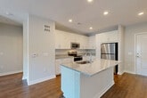 Located at 7105 Hall Rd in Union City, GA, this well-appointed 2-bedroom, 2-bathroom single-floor residence offers a clean, contemporary design with thoughtful finishes throughout. The heart of the home is an open-concept living, dining, and kitchen area bathed in natural light, anchored by a central kitchen island with a granite countertop and undermount sink. The kitchen is equipped with stainless steel appliances — including a range, microwave, and refrigerator — complemented by crisp white shaker cabinetry and matching granite countertops along the perimeter. Rich hardwood-style flooring runs throughout the entire residence, adding warmth and continuity. The living area opens to the outdoors through elegant French doors, allowing abundant natural light and outdoor views. Both bedrooms are generously sized, each featuring large windows with outdoor views and ceiling fans for comfort. The primary bedroom connects to a well-designed en-suite bathroom with a granite vanity, white cabinetry, and direct access to a walk-in closet with wire shelving. Four closets in total provide ample storage. Additional conveniences include a dedicated laundry area and utility room, rounding out this efficiently designed and move-in-ready residence.