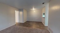 Located at 701 N Indiana Ave in Lubbock, Texas, this single-story home offers a clean and functional layout designed for comfortable everyday living. The interior is finished in neutral gray tones throughout, creating a calm and cohesive atmosphere from room to room. The main living area showcases a combination of durable hardwood-style plank flooring and plush carpet, providing both practicality and warmth underfoot. A textured ceiling adds a classic residential touch, while a flush-mount ceiling light fixture provides straightforward overhead illumination. White trim and baseboards offer crisp contrast against the soft gray walls. A built-in shelving niche adds a subtle architectural detail, ideal for display or storage. A doorway visible from the main living space leads to additional rooms, suggesting a practical and connected floor plan. The HVAC vent in the ceiling points to a central air system for year-round climate control. Overall, the space presents a move-in ready feel with understated finishes that offer a versatile backdrop for a variety of interior styles and furnishing preferences.