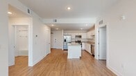This single-floor, 3-bedroom, 2-bathroom residence offers a thoughtfully designed layout that maximizes functionality and comfort. The open-concept kitchen and living area serves as the heart of the home, featuring warm wood-look flooring that flows seamlessly throughout. The kitchen is outfitted with crisp white shaker cabinetry, granite-look countertops, stainless steel appliances including a refrigerator with ice maker, range, microwave, and dishwasher, as well as a central island that provides additional prep space and a double-basin stainless steel sink along the perimeter. Recessed lighting illuminates the space efficiently. The living area extends naturally from the kitchen, offering an open and airy feel enhanced by natural light from large windows. The primary bedroom provides a comfortable retreat of generous size, while two additional bedrooms offer flexibility for various needs. The bathrooms are finished in clean, neutral tones, with one featuring a sliding glass-door walk-in shower with white tile surround. A dedicated laundry room houses a full-size washer and dryer alongside built-in wire shelving for additional storage. Two closets and a connecting hallway round out this efficiently planned, move-in-ready residence.