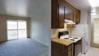 This single-floor unit presents a practical, open-concept layout where the kitchen and living area connect seamlessly. The kitchen is equipped with rich, dark wood cabinetry offering ample upper and lower storage, complemented by light wood-toned laminate countertops. A white electric coil-burner range sits beneath an integrated range hood, providing a functional cooking setup. The cabinetry's warm tones create a grounded, classic aesthetic throughout the kitchen.

Adjacent to the kitchen, the carpeted living area offers a comfortable, open space with neutral gray carpeting and light-colored walls that contribute to a clean, understated ambiance. A sliding glass door at the far end of the living area floods the space with natural light and provides direct access to a balcony, where a railing is visible, suggesting an outdoor area ideal for fresh air and additional light. The overall design reflects a straightforward, functional layout suited for everyday living, with the kitchen and living areas working in tandem to maximize the utility of the available space.