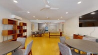 Located at 2075 Lavista Rd NE in Atlanta, GA, this single-floor amenity space offers a thoughtfully designed layout encompassing a fitness center, dining area, two bathrooms, a laundry room, and a connecting hallway. The exercise room serves as the centerpiece, featuring durable rubberized flooring in a striped pattern, a wall of mirrors, and an extensive array of equipment including a multi-station cable machine, free weights, dumbbells, cardio machines, and a weight bench. A sliding barn door leads to a dedicated storage alcove for medicine balls and kettlebells, while French doors open to an outdoor pool area, flooding the space with natural light. Ceiling fans and a wall-mounted AC unit ensure year-round comfort. The dining area transitions naturally from the fitness space, showcasing warm bamboo flooring, a large farmhouse-style wooden table, and a kitchenette with stainless steel appliances, shaker cabinetry, and a geometric tile backsplash illuminated by pendant lighting. A separate seating nook with a round table and open shelving unit adds a lounge feel. The two bathrooms are finished in crisp white tile with large-format floors, modern vanities, and glass-enclosed showers. The laundry room houses commercial-grade washer and dryer units for added convenience.