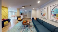 Located at 865 Bellevue Rd in Nashville, TN, this single-floor space is a thoughtfully designed communal area that blends vibrant style with functional versatility. The open-concept layout flows seamlessly across rich hardwood flooring, unified by crisp white walls, crown molding, and recessed lighting that keeps the space bright and welcoming.

The main lounge area anchors the space with a generous navy sectional sofa, an eye-catching teal patterned area rug, and a sculptural wood coffee table. A bold geometric accent wall and a mounted flat-screen TV create a dedicated media viewing nook, while a pair of colorful abstract circular artworks adds to the energetic aesthetic.

Adjacent to the lounge, a bar area features a granite countertop, textured cabinetry, and vivid orange bar stools beneath a striking black cage pendant light. Large French doors nearby invite natural light and provide access to the outdoors. A game room zone, defined by a bright yellow diamond-patterned accent wall, accommodates a billiards table and additional casual seating. Built-in bi-fold storage closets offer practical organization without disrupting the design flow. Structural columns are integrated throughout, adding architectural character. The overall ambiance is modern, lively, and highly functional — ideal for social gatherings and entertainment.