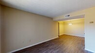 This single-floor, 2-bedroom, 1-bathroom unit features a consistent design language carried throughout its rooms. Dark hardwood-style flooring contrasts with warm neutral, beige-toned walls, creating a cohesive look across the living areas and bedrooms. Textured popcorn ceilings are present throughout, adding a classic architectural detail.

The living area is generously proportioned, offering an open layout that flows into a dedicated dining area, distinguished by a hanging chandelier-style light fixture. A large sliding glass door with vertical blinds allows abundant natural light into the living space and provides access to the exterior.

Both bedrooms are well-sized, each featuring the same dark flooring and neutral walls. Windows fitted with horizontal blinds bring in natural light and outdoor views. The rooms offer ample wall space, providing flexibility for furniture arrangement.

The unit is served by a central HVAC system with ceiling vents visible throughout, ensuring climate control in each room. Clean white baseboards trim the flooring edges consistently across all spaces. Overall, the unit presents a functional and straightforward layout well-suited for comfortable everyday living.