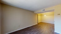 This single-floor, 2-bedroom, 1-bathroom unit features a consistent design language carried throughout its rooms. Dark hardwood-style flooring contrasts with warm neutral, beige-toned walls, creating a cohesive look across the living areas and bedrooms. Textured popcorn ceilings are present throughout, adding a classic architectural detail.

The living area is generously proportioned, offering an open layout that flows into a dedicated dining area, distinguished by a hanging chandelier-style light fixture. A large sliding glass door with vertical blinds allows abundant natural light into the living space and provides access to the exterior.

Both bedrooms are well-sized, each featuring the same dark flooring and neutral walls. Windows fitted with horizontal blinds bring in natural light and outdoor views. The rooms offer ample wall space, providing flexibility for furniture arrangement.

The unit is served by a central HVAC system with ceiling vents visible throughout, ensuring climate control in each room. Clean white baseboards trim the flooring edges consistently across all spaces. Overall, the unit presents a functional and straightforward layout well-suited for comfortable everyday living.