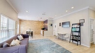 Located at 10010 Skinner Lake Dr in Jacksonville, FL, this single-floor business center offers a thoughtfully designed layout comprising a living room, dining room, and private office. Light-toned wood-look tile flooring flows seamlessly throughout, creating a cohesive and airy atmosphere across the space.

The welcoming entryway features a classic white paneled door topped with an arched transom window, flooding the foyer with natural light. A glass-paneled partition wall separates the private office, which is visible from the entry and offers a calm, professional setting.

The open living area is anchored by a sleek sofa and a teal area rug, complemented by recessed lighting, crown molding, and a wall-mounted flat-screen TV. Adjacent to the living area, the dining room is a standout space featuring a striking whitewashed stacked-stone accent wall, arched windows overlooking a lush outdoor setting, and a communal table with industrial-style seating — ideal for collaborative gatherings.

A secondary seating area with a white table and modern lattice-back chairs sits beside a built-in shelving unit and an additional wall-mounted display screen. Natural light pours in from multiple windows throughout, reinforcing the space's bright, clean, and inviting character. The overall aesthetic is contemporary and functional, well-suited for community or professional use.