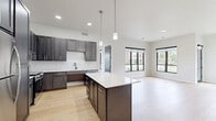 Located at 582 Larson Orchard Pky in Hobart, WI, this well-appointed single-floor home offers three bedrooms, two bathrooms, and a thoughtfully designed open-concept layout. The kitchen and living area serve as the heart of the home, featuring light hardwood flooring, dark gray shaker-style cabinetry, white quartz countertops, stainless steel appliances, and a central island illuminated by pendant lighting. Recessed ceiling lights add to the bright, clean aesthetic throughout. The living area extends the open feel with additional windows overlooking the surrounding neighborhood. Each bedroom is carpeted for comfort and fitted with bold black-framed windows that flood the rooms with natural light and provide views of the landscaped grounds. The primary bedroom offers a generous footprint with dual-window exposure. The bathrooms feature modern dark vanities with white countertops and light tile flooring. One bathroom includes a walk-in shower with a full-surround enclosure, while the second is ADA-accessible, equipped with safety grab bars, a comfort-height toilet, and a sleek undermount sink vanity with a framed mirror. A dedicated closet completes the floor plan, adding practical storage to this clean, contemporary home.