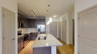 This single-story residence offers a thoughtfully designed layout that balances functionality and modern style. The kitchen serves as a central highlight, showcasing rich dark-espresso cabinetry that extends to the ceiling for ample storage, light granite countertops, and a full suite of stainless steel appliances including a French door refrigerator, electric range, and built-in microwave. A large kitchen island with an undermount sink and pendant lighting above creates an ideal space for both meal preparation and casual dining. Track lighting throughout the main living areas adds a contemporary touch.

The open living area flows naturally from the kitchen, featuring warm wood-style flooring, a ceiling fan with light fixture, and access to a private exterior door. Natural light filters in through multiple windows fitted with blinds. The bedroom continues the wood-style flooring and includes a ceiling fan, track lighting, and a window for natural light.

The bathroom is finished with matching granite countertops on the dark vanity, a tiled tub-shower combination, and wood-style flooring. An adjacent walk-in closet provides generous storage. The overall design is cohesive, clean, and modern throughout.