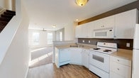 This three-floor property in Hamburg offers a practical and well-organized layout designed for comfortable everyday living. The kitchen serves as a functional hub, featuring white cabinetry with ample storage, light-toned countertops, a double-basin sink, and a full suite of white appliances including a range with coil burners, an over-the-range microwave, dishwasher, and refrigerator. A bold accent wall in a warm taupe tone adds visual contrast against the crisp white cabinetry. The kitchen opens directly to the living area via a peninsular breakfast bar, creating a seamless, connected flow between spaces. The living areas are finished with neutral-toned carpet, while the kitchen and wet areas feature wood-look hard flooring. Ceiling fans are installed in the main living spaces, contributing to air circulation and comfort. Multiple windows fitted with horizontal blinds allow generous natural light to filter throughout. A separate room with exterior door access opens to an outdoor view, providing flexible use as a dining or additional living space. The bathrooms include a full bath with a soaking tub and shower combination, as well as a compact half bath with a vanity. A dedicated laundry room accommodates a full-sized washer and dryer with wire shelving overhead.