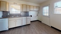 This single-story home offers a practical and comfortable layout designed for everyday living. The galley-style kitchen is well-equipped with ample cream-toned cabinetry, laminate countertops, a gas range, a full-size refrigerator, and a double-basin sink. Natural light filters in through a window above the sink, and durable wood-look vinyl flooring runs throughout the kitchen and utility areas. A secondary kitchen view reveals additional counter space, a double sink, and a door providing convenient exterior access.

The living area features a seamless blend of wood-look flooring and plush carpeting, with a sliding glass door that opens directly to a fenced backyard patio, filling the space with natural light and outdoor views. Multiple bedrooms are finished with soft wall-to-wall carpeting and feature windows with blinds that provide both natural light and privacy. The primary bedroom is outfitted with a ceiling fan and light fixture for added comfort.

The bathroom is finished with warm earth-toned tile walls, a white vanity with under-cabinet storage, a framed mirror, and a towel bar. The floor plan, visible in the dollhouse view, reveals a well-organized layout with clearly defined living, sleeping, and kitchen zones throughout the home.