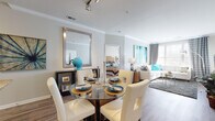 This single-floor residence offers a thoughtfully designed open-concept layout that seamlessly connects the living, dining, and kitchen areas. The living room is a welcoming space featuring crown molding, wood-look flooring, and a patio door that invites natural light. The dining area accommodates a round glass table and is accented by a large framed mirror, while the adjacent living space provides ample room for relaxing and entertaining.

The kitchen is outfitted with dark espresso cabinetry, granite countertops, a subway tile backsplash, stainless steel appliances including a refrigerator, range, and built-in microwave, and a kitchen island offering additional prep and seating space.

The residence includes multiple bedrooms, each with plush carpeting, generous windows with natural light, and room for substantial furniture. One bedroom features a ceiling fan, while another offers a four-poster bed frame, lending a classic touch.

Two full bathrooms serve the residence. The primary bathroom features a long double-sink vanity with dark cabinetry and well-lit mirrors. The secondary bathroom includes a single-sink vanity with matching dark cabinetry and a tub-shower combination, both finished with wood-look flooring. The overall aesthetic is modern and cohesive, with neutral tones accented by teal and white décor throughout.