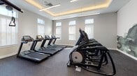 The Grove Fitness Center in Piscataway, NJ is a thoughtfully designed, single-floor facility that offers a comprehensive workout experience across multiple well-defined zones. The interior features a clean, contemporary aesthetic with neutral gray walls, rubber flooring, and a tray ceiling accented by warm cove lighting complemented by sleek linear fixtures overhead.

The cardio area is lined with a row of treadmills and elliptical machines positioned along large windows fitted with white blinds, allowing ample natural light to fill the space while providing a bright, energizing atmosphere. Adjacent to this is the strength training area, which is generously outfitted with Matrix-brand cable machines, weight benches, a full dumbbell rack, and a variety of selectorized machines — all arranged to maximize floor space and ease of use. Full-length mirrors along the walls visually expand the room and allow users to monitor their form.

A dedicated cycling studio rounds out the facility, housing multiple stationary bikes with individual mounted screens for interactive workout sessions. This area also benefits from tall windows and wall-mounted mirrors, creating an open, motivating environment. Throughout the fitness center, the combination of modern equipment, strategic lighting, and natural light fosters a professional and welcoming space suited for a wide range of fitness routines.