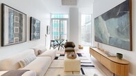 Located in the heart of downtown Montréal, this modern 2-bedroom, 2-bathroom residence offers a thoughtfully designed open-concept layout with clean lines and contemporary finishes. A welcoming entrance hallway with light hardwood flooring and a floating wood console table leads into the heart of the home. The combined kitchen and dining area is anchored by a sleek island with bar seating, two-tone cabinetry in warm wood and white, a gray tile backsplash, and stainless steel appliances. A pendant light adds a stylish focal point overhead. The living and dining space benefits from expansive floor-to-ceiling windows that flood the area with natural light and frame open city views of the Montréal skyline. Both bedrooms are bright and well-proportioned, each featuring large windows with urban views and dedicated closet space. The primary bedroom offers a serene retreat with a restful atmosphere. The two bathrooms are finished with gray subway tile — one featuring a frameless glass walk-in shower, and the other a full soaking tub. In-unit laundry and three closets add practical convenience. Light hardwood floors, white walls, and modern fixtures carry a cohesive, minimalist aesthetic throughout the entire residence.