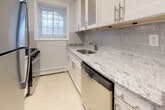 Located at 401 E Jericho Tpke in Carle Place, NY, this single-floor unit offers a thoughtfully designed layout with quality finishes throughout. The renovated kitchen is a standout feature, showcasing granite countertops with striking veining, white shaker cabinetry with brushed nickel hardware, a classic subway tile backsplash, stainless steel appliances including a gas range and dishwasher, and light tile flooring. The bathroom has been fully updated with white subway tile extending from floor to ceiling, a marble-topped vanity with brushed bronze fixtures, a mirrored medicine cabinet, a soaking tub with shower, and natural light provided by a window. The living areas and bedrooms feature warm, polished hardwood floors that carry consistently throughout the unit, complemented by soft blue-gray walls and crisp white trim and baseboards. Several rooms are generously proportioned, with large windows that invite natural light and offer views of the surrounding greenery. Each room is equipped with baseboard heating, and select rooms also include wall-mounted air conditioning units for year-round comfort. Closet storage is available in the bedrooms, and the overall layout provides a functional flow from room to room. The unit presents a clean, move-in-ready environment with modern updates balanced by classic finishes.