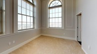 This single-floor unit combines classic architectural details with modern finishes throughout its well-appointed layout. The bedroom is a standout space, characterized by soaring ceilings and dramatic arched windows topped with elegant fanlight transoms. These oversized windows flood the room with abundant natural light and offer views of the surrounding streetscape. Neutral-toned carpet and paneled wall moldings lend a refined, traditional character to the space.

The living area continues the bright, open feel with large multi-pane windows, warm hardwood-style flooring, and elevated ceilings fitted with recessed and pendant lighting. A louvered closet provides practical storage, while the open-plan layout connects seamlessly to the kitchen.

The kitchen is equipped with dark espresso cabinetry, dark granite countertops, and black appliances including a refrigerator, range, and built-in microwave. A peninsula with an integrated stainless steel sink and pendant lighting above creates a functional and stylish focal point.

The bathroom features slate-toned tile flooring, a pedestal sink, a tub-shower combination, and a bright window that allows natural light. A dedicated laundry area with washer and dryer hookups and a carpeted walk-in closet complete this well-designed unit.