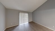 Located at 1817 E Oltorf St in Austin, TX, this one-bedroom, one-bathroom unit offers a practical and well-organized single-floor layout. The living room features wood-style flooring, vaulted ceilings, and a sliding glass door dressed with vertical blinds that allows natural light to fill the space. A ceiling fan with a light fixture adds comfort and functionality to the room. The open layout flows into a dedicated dining area, highlighted by a trio pendant light fixture and neutral gray walls, seamlessly connecting to the kitchen. The galley-style kitchen is well-equipped with white cabinetry, gray laminate countertops, a double stainless steel sink, and black appliances including a gas range and refrigerator, providing ample storage and prep space. The spacious bedroom features its own sliding glass door with vertical blinds, wood-style flooring, a ceiling fan, and a walk-in closet with built-in rod. The bathroom is clean and functional, featuring a full tub-shower combination with white tile surround and updated fixtures. Textured ceilings are consistent throughout, and the neutral gray color palette lends the space a cohesive, modern feel. A hallway connects the main living areas to the private quarters.